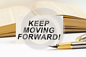 Against the background of the book lies a pen and a business card with the inscription - KEEP MOVING FORWARD