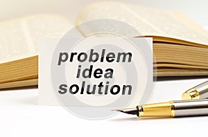 Against the background of the book lies a pen and a business card with the inscription - problem idea solution