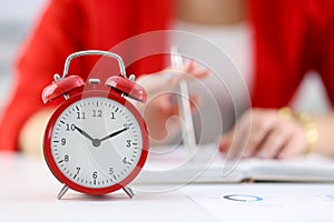 Against the background of businesswoman stands red alarm clock