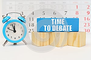 Against the background of the calendar is an alarm clock, cubes and a blue block with the inscription - Time to Debate