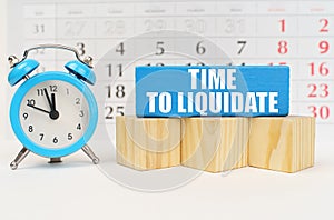 Against the background of the calendar is an alarm clock, cubes and a blue block with the inscription -Time to Liquidate