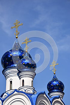 Against the background of a clear blue sky, there are several domes of a Christian church of various sizes, with crosses at the