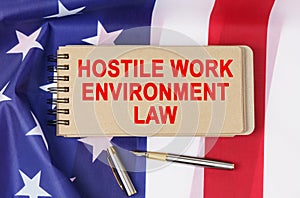 Against the background of the flag of the USA lies a notebook with the inscription - HOSTILE WORK ENVIRONMENT LAW