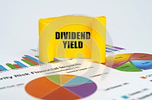 Against the background of graphs and charts, a yellow paper plate with the inscription - DIVIDEND YIELD