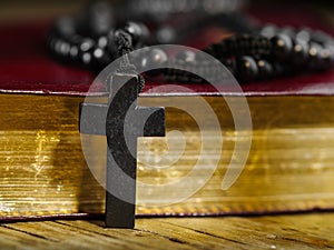 Against the background of the Holy Bible lie a Catholic rosary and a cross. Macro shot. There are no people in the photo.