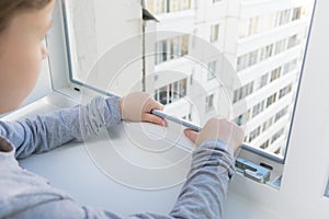 against the background of the house, the childs hands holding the edge of the window frame