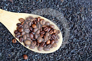 against the background of loose tea lies a wooden spoon with coffee beans