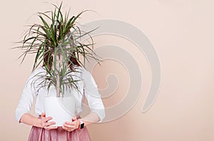 Against the background of milky coffee color, the girl is holding a potted plant in her hands. Girl`s face is covered by a plant