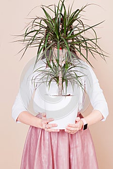 Against the background of milky coffee color, the girl is holding a potted plant in her hands. Girl`s face is covered by a plant