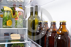 Against the background of an open white refrigerator, bottles of wine, beer and glass jugs with soft drinks of their citrus fruits