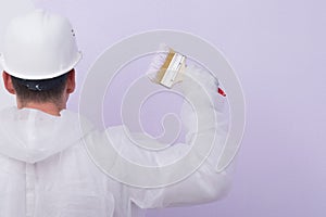 Against the background of a painted wall, a worker`s hand holding a brush, rear view