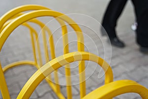 Against the background of paving stones and human feet, Parking for bicycles. Yellow metal close-up with space for