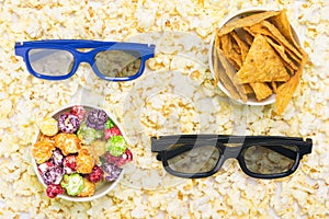 Against the background of popcorn grains two cups with different flavors of corn and glasses for the cinema