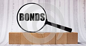 Against the background of reports on wooden cubes - a magnifying glass with the text BONDS. Business concept