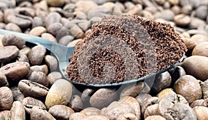Against the background of roasted aromatic coffee beans lies a metal spoon filled with ground coffee. A drink made from