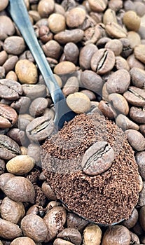 Against the background of roasted aromatic coffee beans lies a metal spoon filled with ground coffee. A drink made from