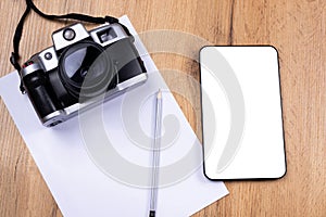 Against the background of the desk- vintage photo camera, digital tablet with a white mock up screen, a blank white sheet for