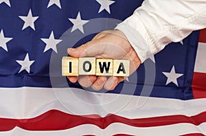 Against the background of the USA flag, a man& x27;s hand with cubes with the text - IOWA