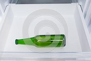 Against the background of a white refrigerator drawer, one glass bottle of beer
