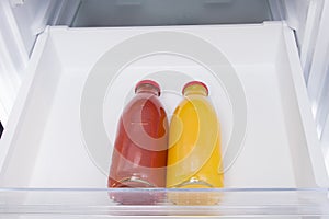 Against the background of a white refrigerator drawer, two glass bottles with juice, close-up