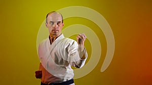 Against a color-changing background, an adult athlete beats, performs punches and blocks with his hands