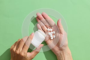 Against the light green background, white pills are poured from a white bottle unlabeled into a palm