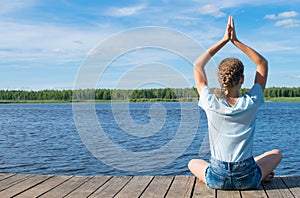 Against the sky, the girl sitting on the pier, doing yoga, outdoors