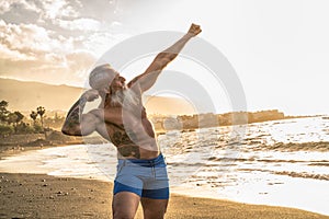 Age is just a number. In a healthy body, healthy mind. Senior man with white stylish beard showing his muscular fit body with photo