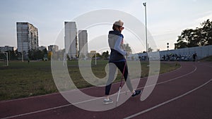 Age maturity, active lifestyle and wellness. Joyful retired woman with walking poles around the city stadium. Mature