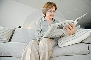 age and people concept - happy senior woman reading newspaper at home