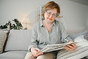 age and people concept - happy senior woman reading newspaper at home