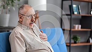 Aged 70s grandfather myocardial infarction symptoms heart attack sitting on blue couch at home