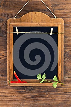 Aged blackboard with chilli peppers and parsley hanging on wooden wall