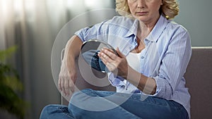 Aged blond lady touching her face looking into a hand mirror, aging process