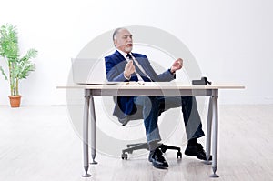 The aged businessman doing yoga exercises in the office