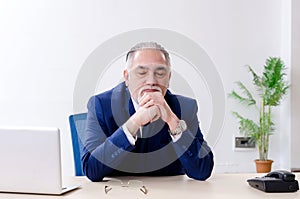 The aged businessman doing yoga exercises in the office