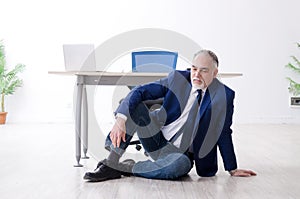 The aged businessman doing yoga exercises in the office