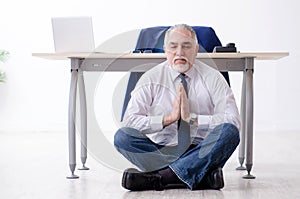 The aged businessman doing yoga exercises in the office