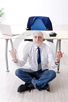 The aged businessman doing yoga exercises in the office