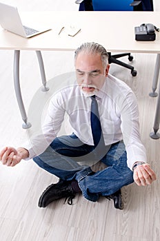 The aged businessman doing yoga exercises in the office