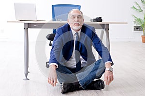 The aged businessman doing yoga exercises in the office