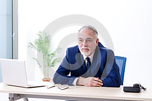 The aged businessman doing yoga exercises in the office