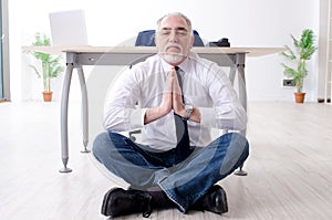 The aged businessman doing yoga exercises in the office