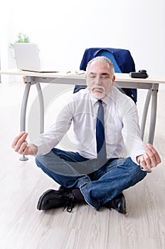 The aged businessman doing yoga exercises in the office