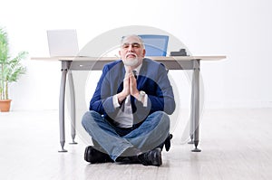 Aged businessman doing yoga exercises in the office