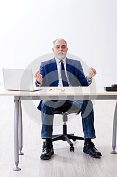 Aged businessman doing yoga exercises in the office