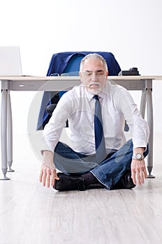 Aged businessman doing yoga exercises in the office