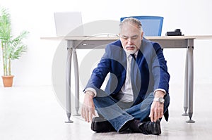 The aged businessman doing yoga exercises in the office