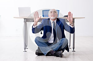 Aged businessman doing yoga exercises in the office