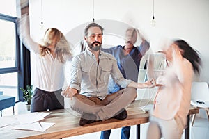 Aged businessman sitting on table and meditating in lotus position while colleagues running around